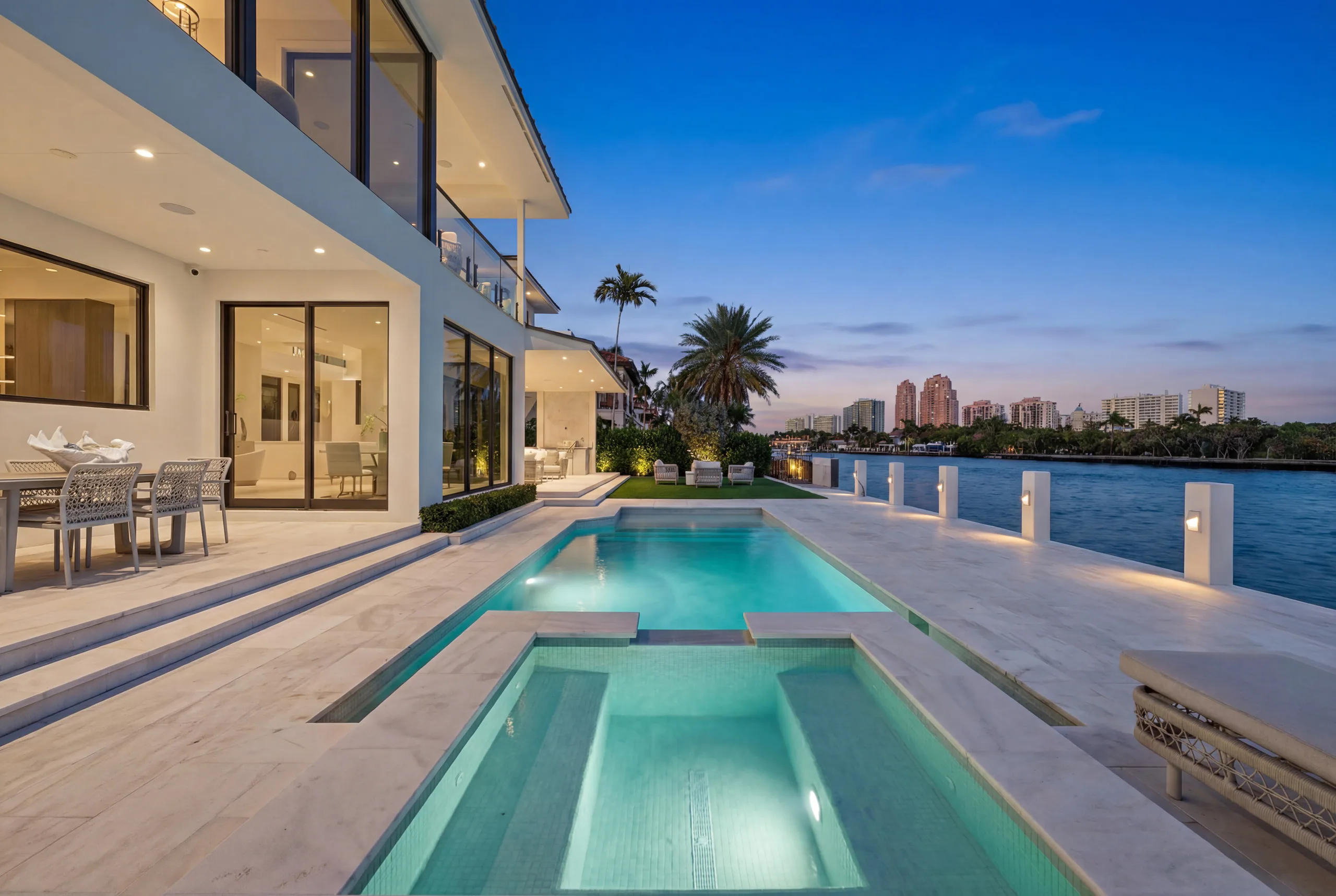 Illuminated pool and waterfront terrace beneath a blue-hour sky